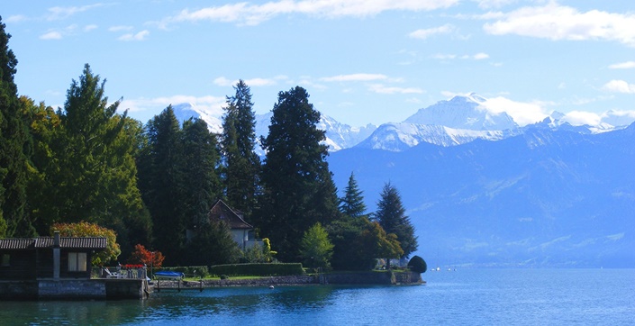 Ufer des Thuner Sees mit schneebedeckten Alpengipfeln im Hintergrund.