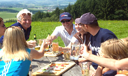 Teilnehmer einer Gruppenreise picknicken auf einer grünen Wiese am Waldrand