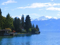 Postkartenidyll mit blauer Wasserfläche und sattgrünen Bäumen vor schneebedeckten Berggipfeln